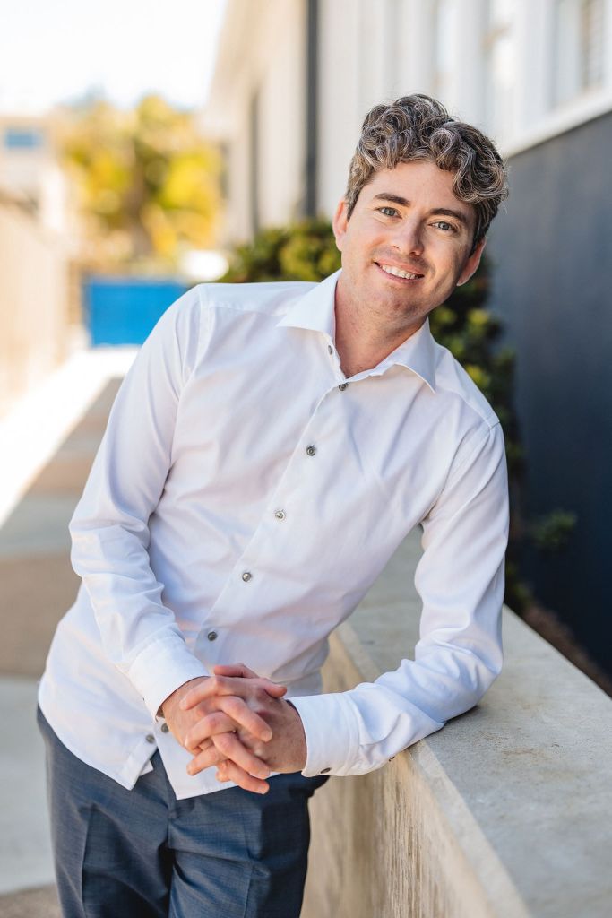 A picture of Matthew, the owner of MP Storytelling, leaning and smiling in a purple shirt and navy blue pants.
