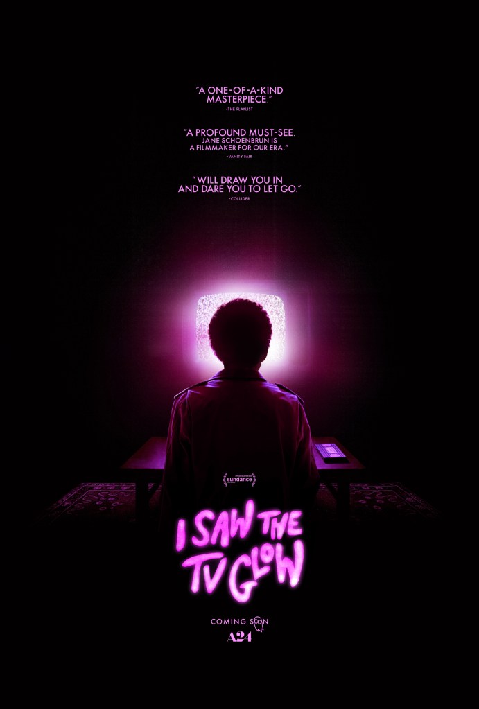 A poster for the film I Saw the TV Glow. It's a picture of the back of the main character Owen (played by Justice Smith) in a dark room looking at a static television glowing pink. Next to him on a table is a VHS tape.